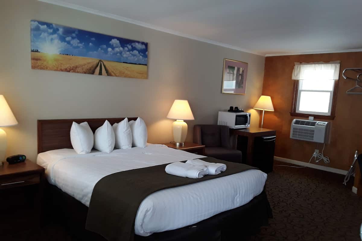 A hotel room with a bed, two bedside lamps, a TV, a microwave, and a window with a curtain.