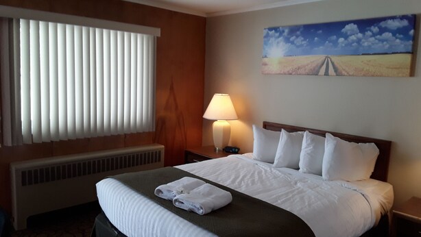 Habitación de hotel con cama, mesita de noche con lámpara, un cuadro en la pared y ventana con persianas.
