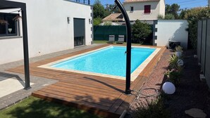 A rectangular swimming pool with a wooden deck, surrounded by a white wall and a green fence. - Modern air-conditioned architect designed villa with private pool  (Le Cannet-des-Maures)