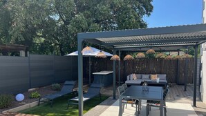 A covered patio area with a table and chairs, a cushioned seating area, and a pergola with hanging lamps. - Modern air-conditioned architect designed villa with private pool  (Le Cannet-des-Maures)