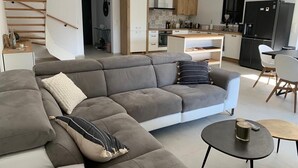 A modern living room with a grey sectional sofa, a small round table, and a staircase. - Modern air-conditioned architect designed villa with private pool  (Le Cannet-des-Maures)