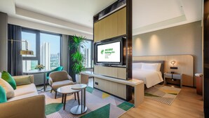 Ein modernes Hotelzimmer mit Bett, Schreibtisch, Stuhl, Fernseher und einem großen Fenster mit Blick auf die Stadt.
