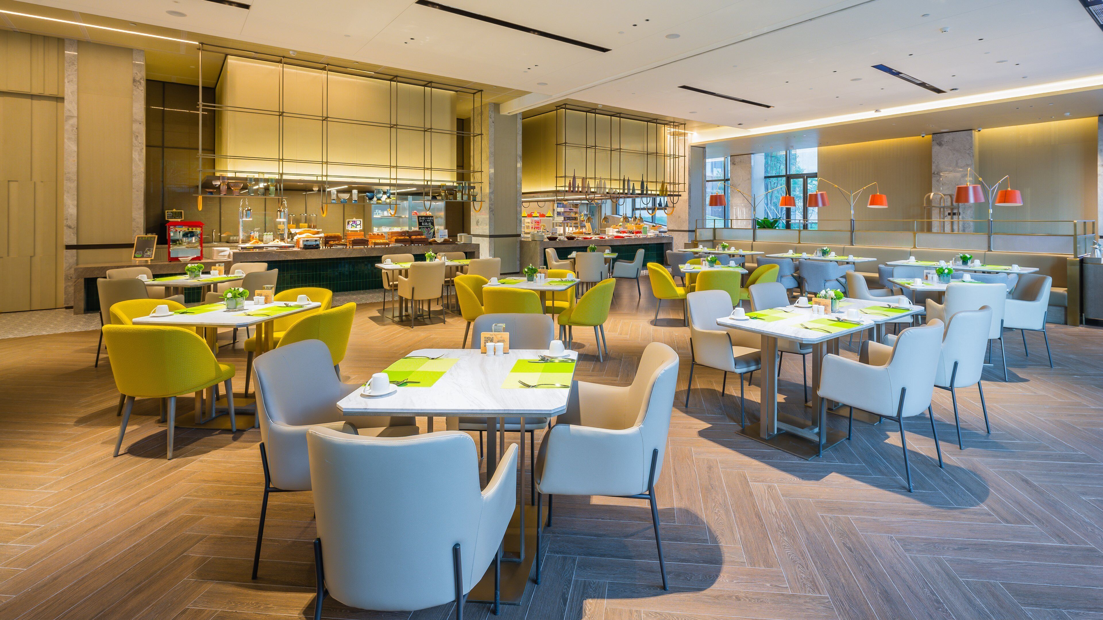 A spacious dining area with multiple tables and chairs, a kitchen in the background, and a modern interior design.