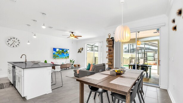 A modern kitchen with a central island, a dining area with a wooden table and chairs, and a living area with a sofa and a TV.