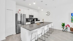 A modern kitchen with white cabinets, stainless steel appliances, a central island with bar stools, and a clock on the wall.