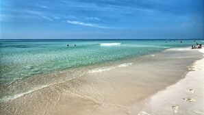 Una playa con agua turquesa cristalina, una orilla arenosa y algunas personas a lo lejos.