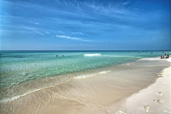 A beach with clear turquoise water, a sandy shore, and a few people in the distance.