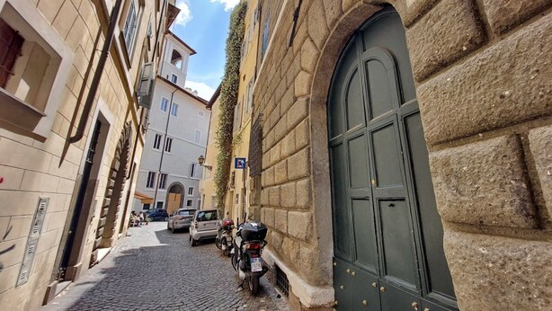 A narrow cobblestone street with buildings on either side, a parked motorcycle, and a green door on the right.