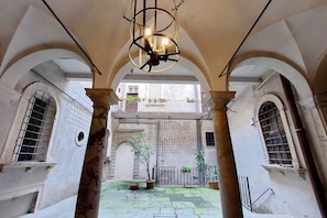 An interior courtyard with arches, a hanging light fixture, and potted plants. - Montevecchio2 - Charming apartment for 4 close to piazza Navona (Roma)