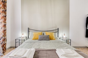 Un lit recouvert d’une couvre-lit à motifs, deux tables de chevet avec des lampes et un rideau orné de motifs de feuilles.