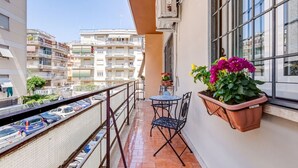 Un balcon avec une table et des chaises, un pot de fleurs suspendu et une vue sur les bâtiments environnants.