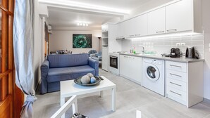 Et moderne køkken med hvide skabe, en vaskemaskine og et spiseområde med en blå sofa og et hvidt bord.