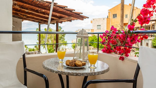 En balkon med et bord dækket til to personer, der viser en tallerken med småkager og to glas appelsinjuice, en dekorativ lanterne og livlige lyserøde blomster.