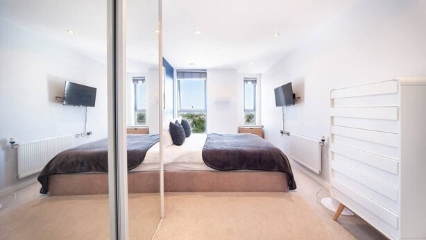 Un dormitorio moderno con dos camas, ventanas amplias y un radiador blanco.