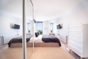 Quarto moderno com duas camas, janelas amplas e radiador branco.