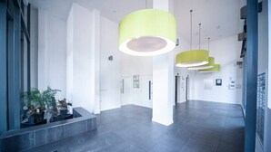 Un vestíbulo moderno con diseño minimalista, que presenta una escalera central, plantas en macetas y una lámpara colgante de color amarillo brillante.