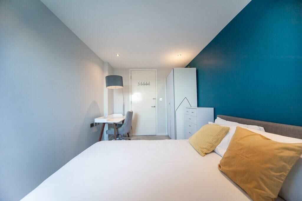 A modern hotel room with a bed, a desk, and a wardrobe.