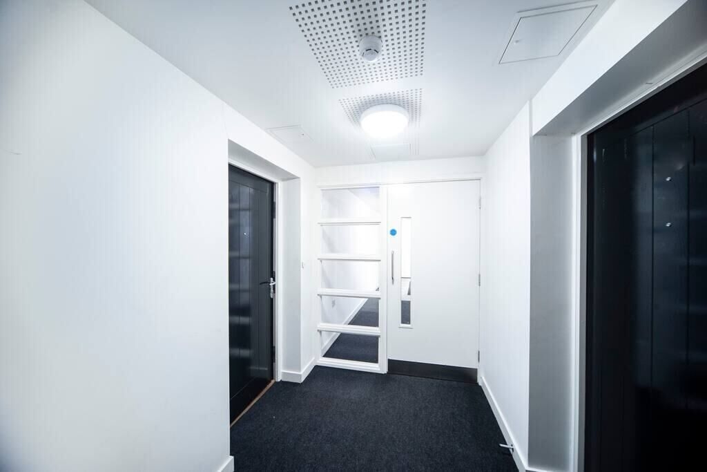 A narrow hallway with a carpeted floor, white walls, and a door with a blue handle.