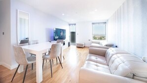 Una sala de estar moderna con un sofá blanco, una mesa de comedor con sillas y un televisor.