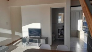 Ein modernes Wohnzimmer mit Flachbildfernseher, einem Esstisch mit Stühlen und Blick in ein angebundenes Badezimmer.
