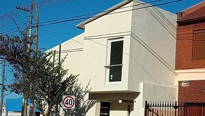 Ein modernes, zweistöckiges Haus mit weißer Fassade, einer schwarzen Tür und einem Fenster.