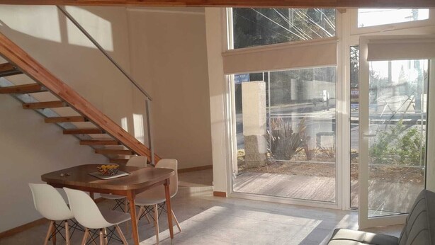 Ein modernes Interieur mit einer Holztreppe, einem Essbereich inklusive Tisch und Stühlen sowie einer großen Schiebeglastür, die zu einem Außenbereich führt.