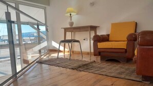 Ein Zimmer mit Holzboden, einem braunen Ledersofa mit gelbem Kissen, einem kleinen Holztisch mit Lampe und einem Sessel.