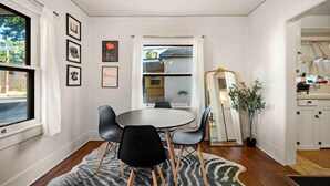 A dining area with a round table, black chairs, a zebra-patterned rug, framed pictures on the wall, and a window with a view of a building and greenery. - Quaint Heart of Downtown Flagstaff Unit w/Spa & AC (Flagstaff)
