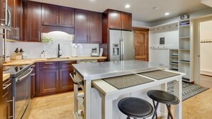 A modern kitchen with dark wooden cabinets, stainless steel appliances, and a central island with stools. - Copper Mtn Condo w/ Heated Pool: Ski-In/Walk-Out! (Frisco)