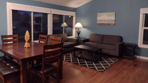 Ein Wohnzimmer mit Esstisch, Stühlen, einer Couch, einem Couchtisch und einer Lampe.
