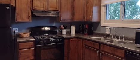 A kitchen with wooden cabinets, a black stove, a sink, and a window with a view of trees.
