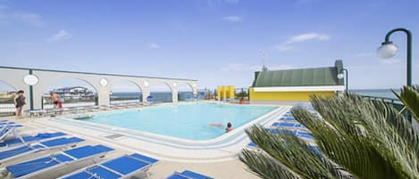 Un área de piscina con sillas reclinables azules, una piscina y un edificio con techo verde.