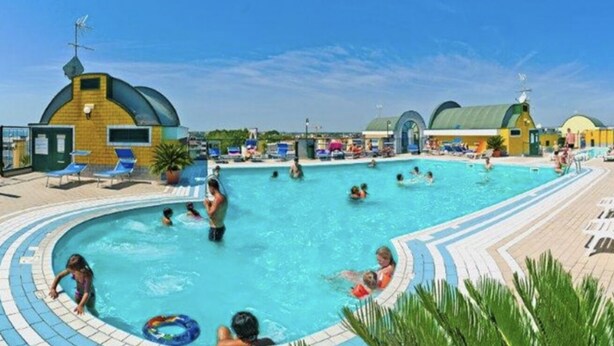 A swimming pool with people enjoying the water, surrounded by lounge chairs and umbrellas.