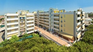 A multi-story hotel with balconies, a swimming pool, and a parking area.