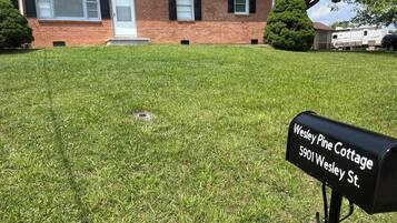 Welcome to Wesley Pine Cottage, a charming home with a front door, small porch, and garage, set amidst a well-manicured lawn and a tree.