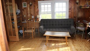 Una stanza con rivestimenti in legno, un divano grigio, un tavolino in legno e una sedia.