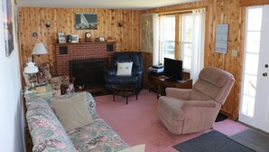 A cozy living room with a fireplace, a leather armchair, a sofa, and a television. - Point Field (Deer Isle)