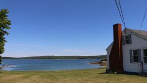 A white house with a red chimney, a dock, and a grassy area by a large body of water. - Point Field (Deer Isle)