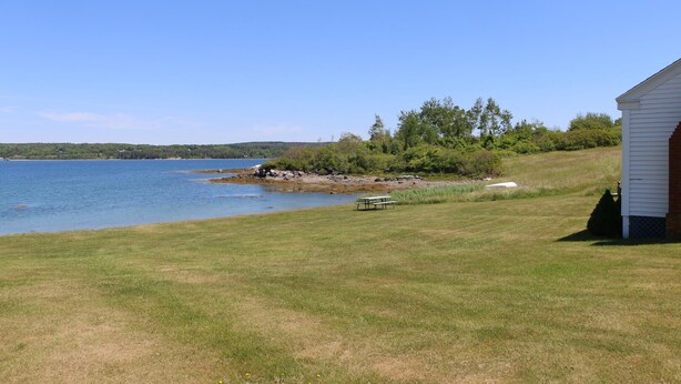 A lakeside property with a grassy lawn, a picnic table, and a small building. - Point Field (Deer Isle)