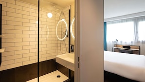 A modern bathroom with a glass-enclosed shower, a white sink, and a mirror with a circular light. - Ibis Marseille Marignane Technopole (Marignane)