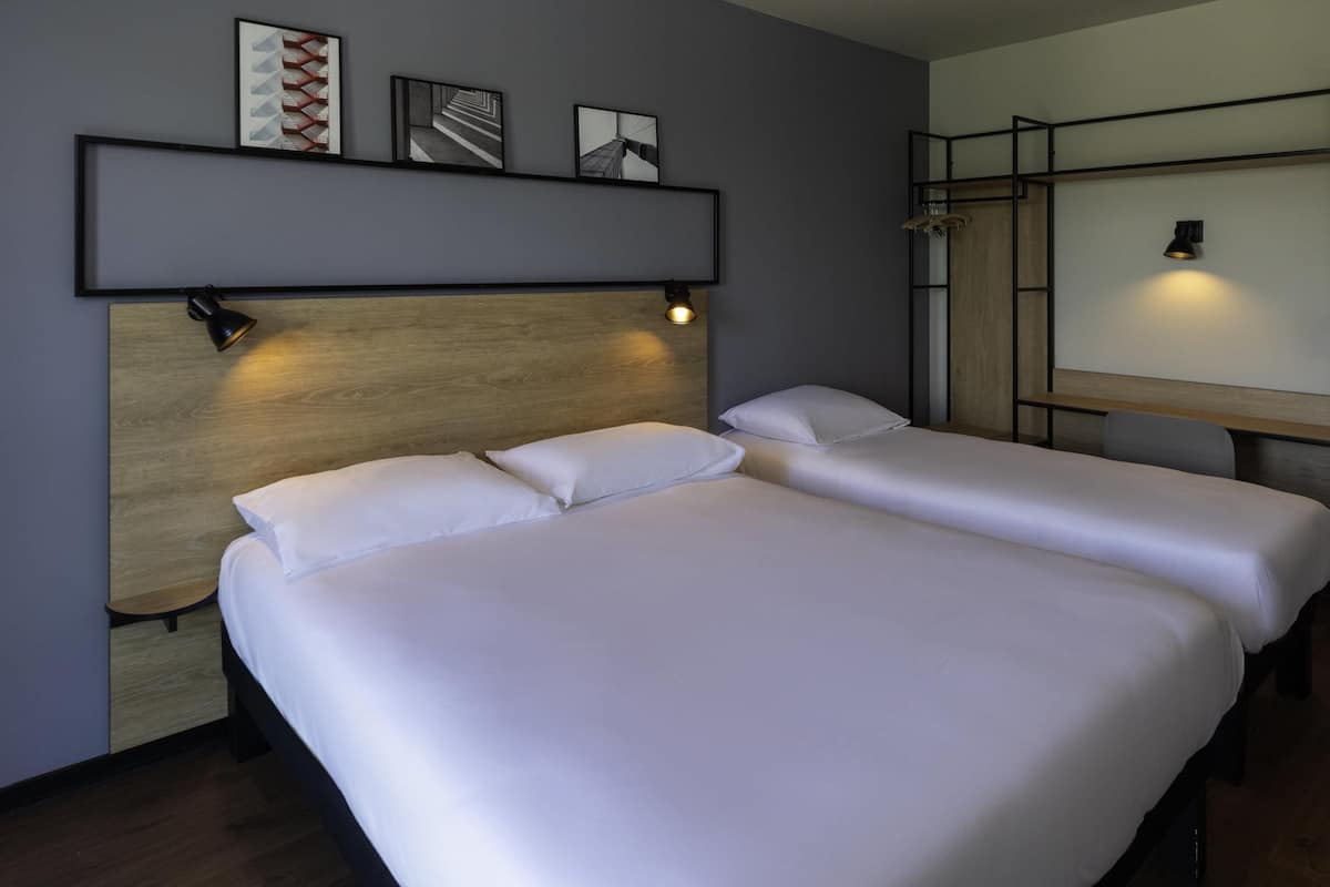 Hotellihuone, jossa on kaksi sänkyä, puinen pääty, hylly kehystettyjä kuvia varten ja työpöytä, jossa on lamppu.