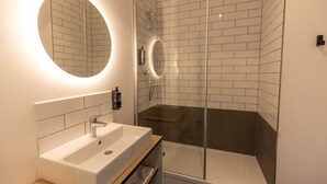 Un baño moderno con lavamanos blanco, un espejo y cabina de ducha con mampara de vidrio.