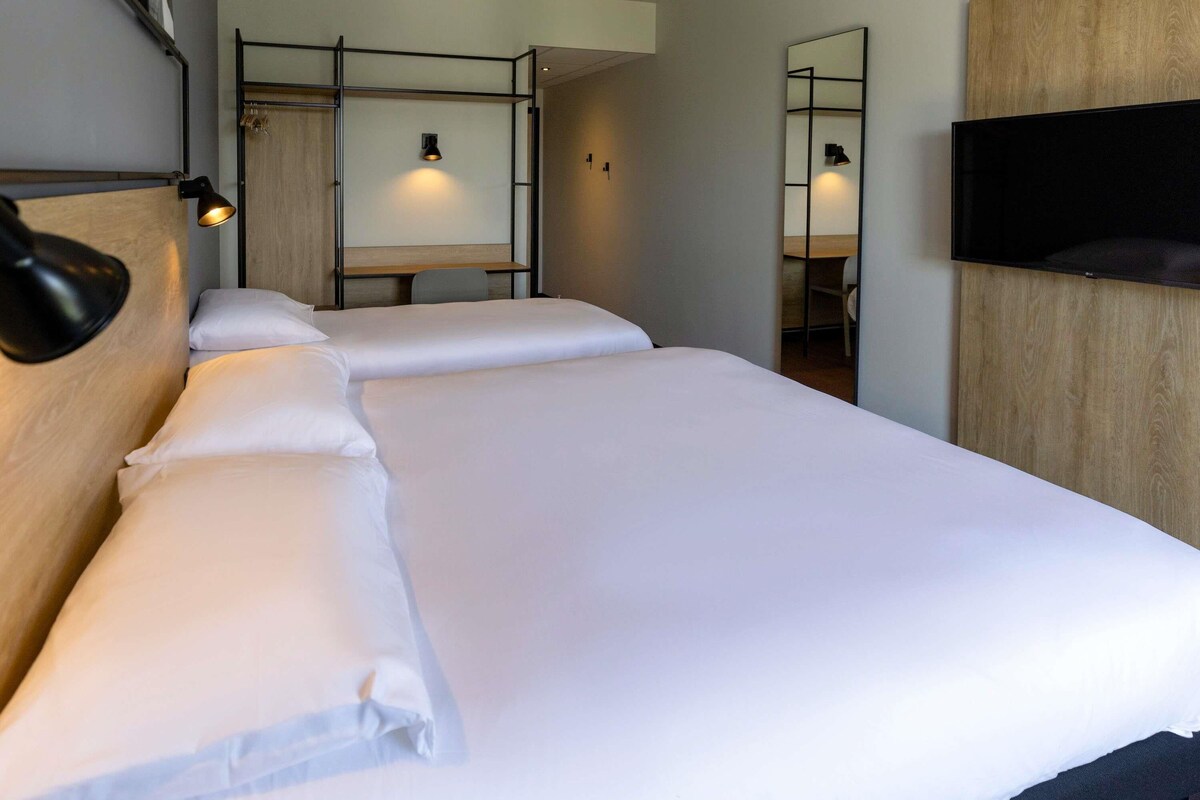 A hotel room with a large bed, a desk, a chair, a TV, and a mirror.