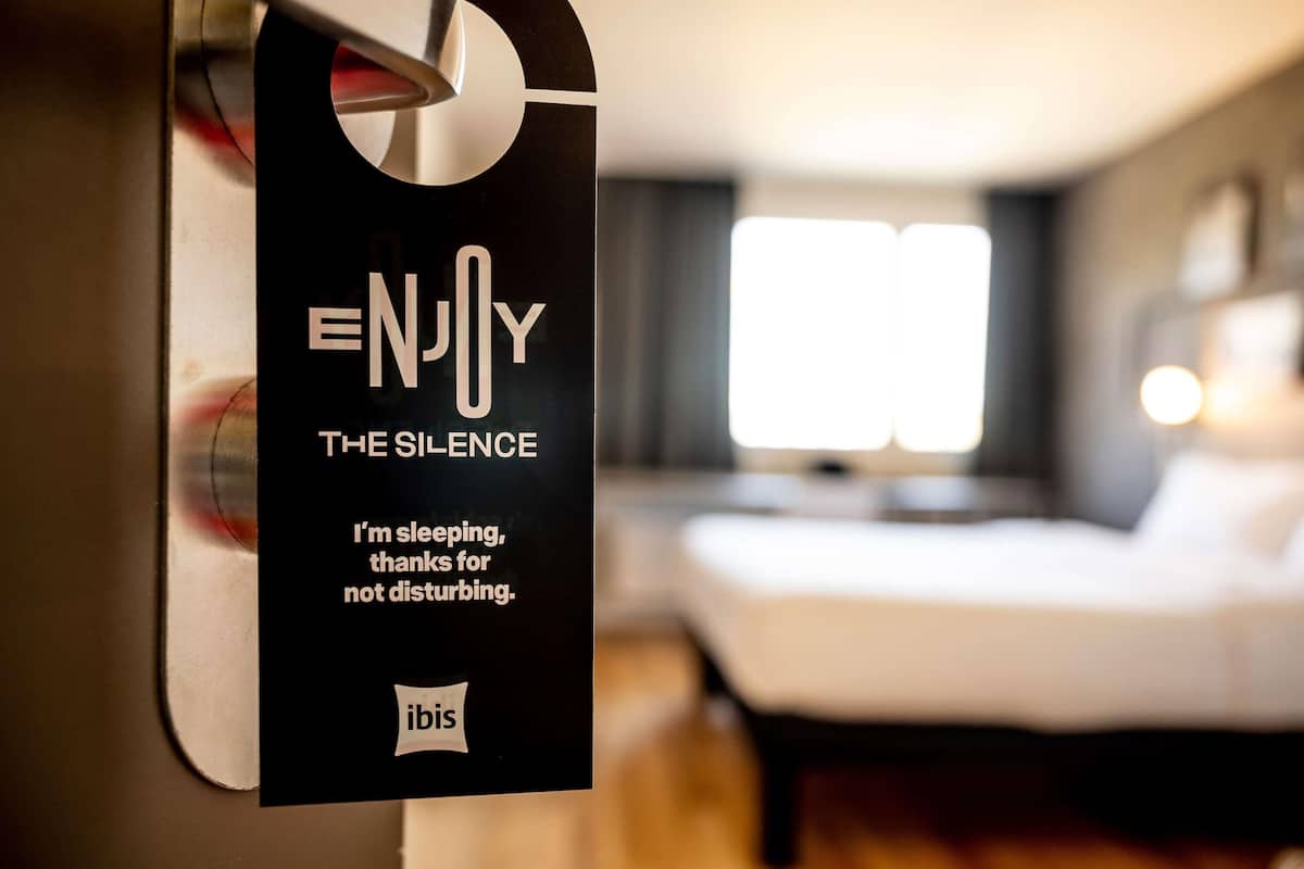 Hotellihuone, jossa on sänky, ikkuna ja kyltti ovessa.