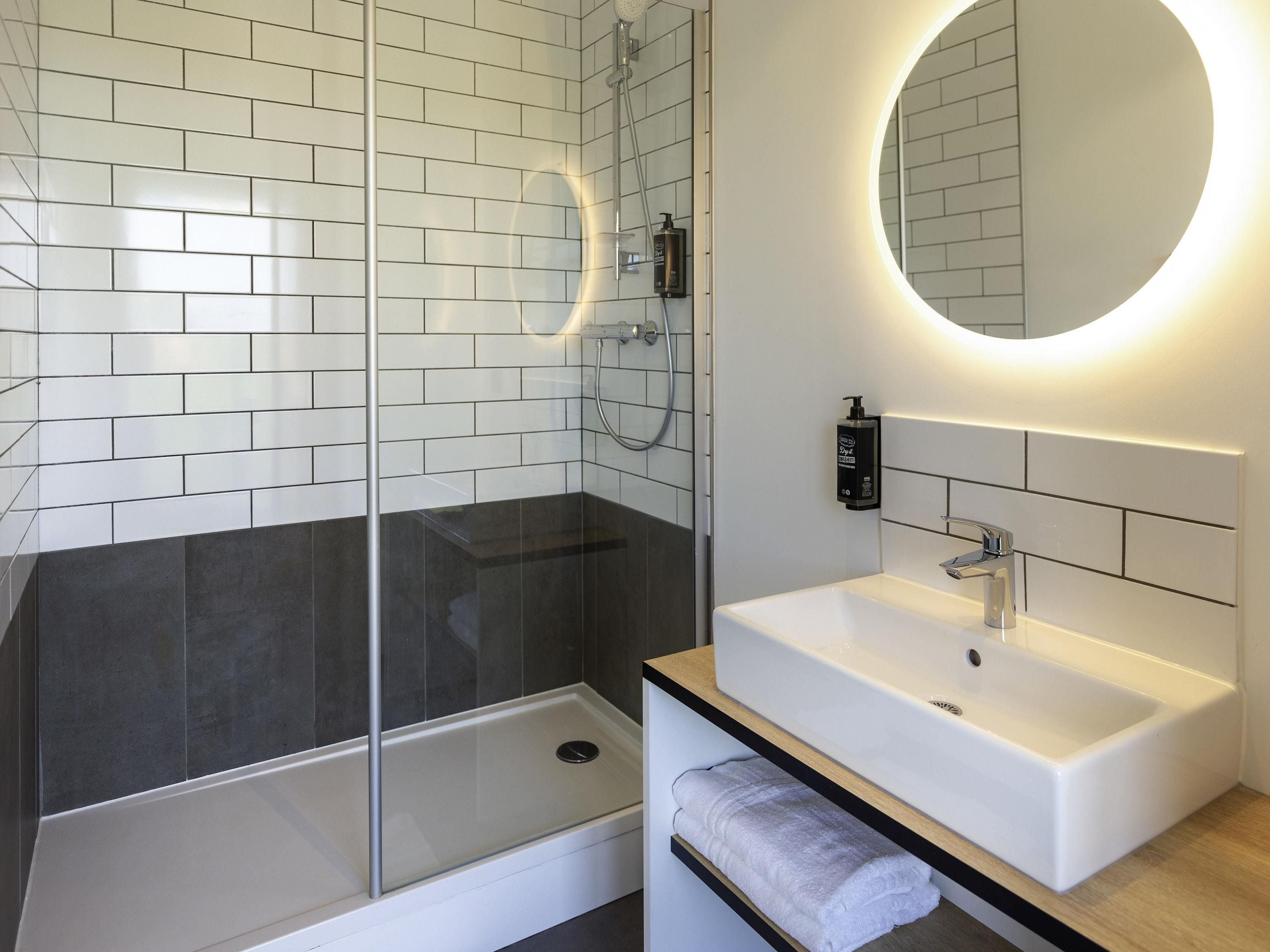 A modern bathroom with a glass-enclosed shower, a white sink with a mirror, and a towel rack.