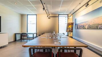 A conference room with a long table, two chairs, a projector screen, and a large window.