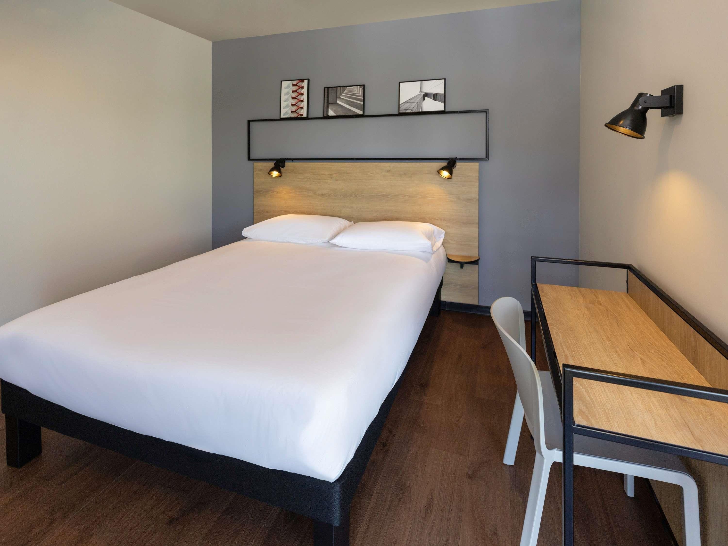 A neatly arranged hotel room with a bed, a desk, and a chair.