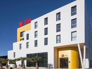 Un hotel moderno con un llamativo logo rojo de 'ibis' en la fachada, múltiples ventanas y una pared de acento amarilla.