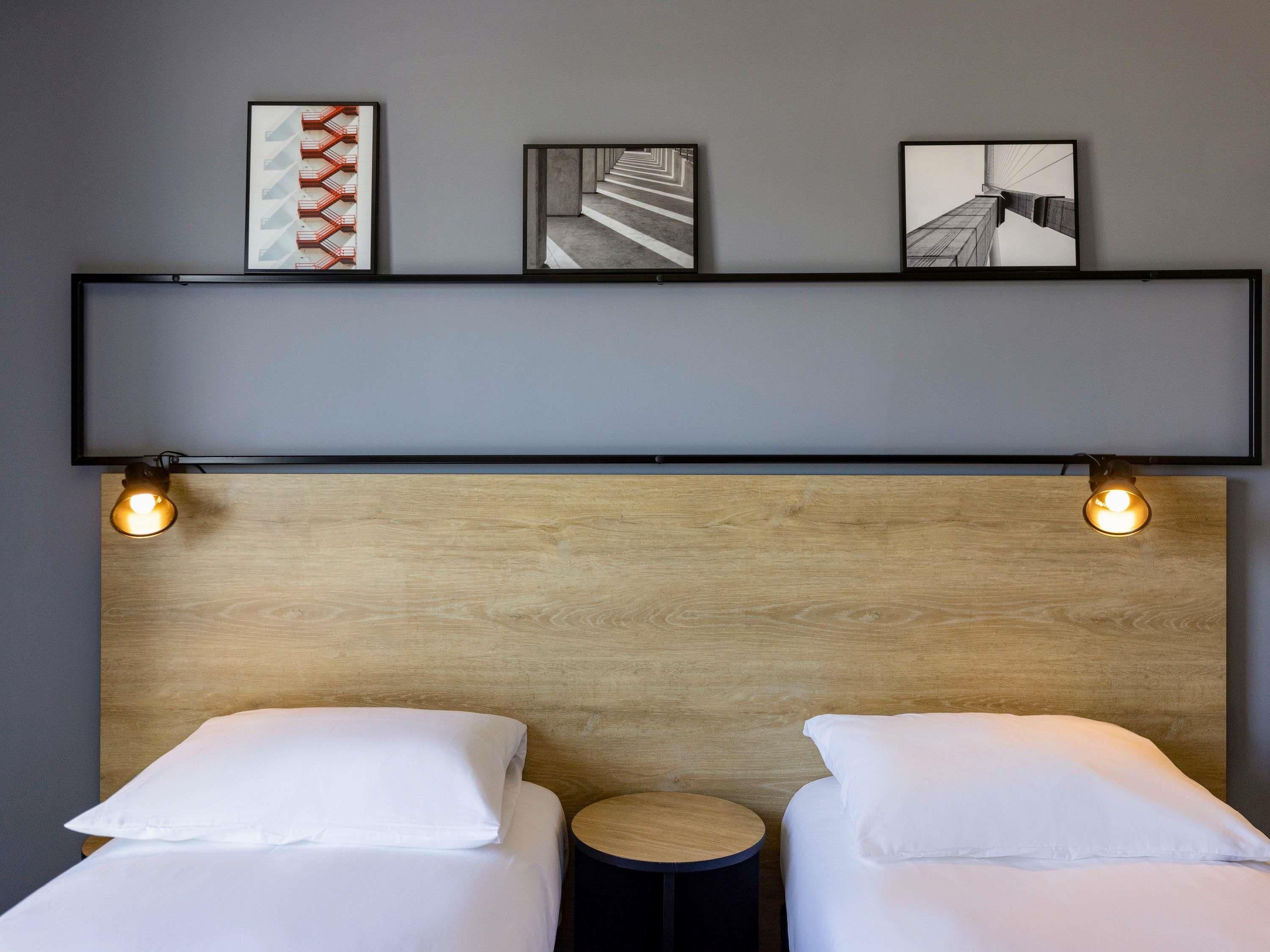 Une chambre d’hôtel avec deux lits, une tête de lit en bois et trois tableaux encadrés accrochés au mur.