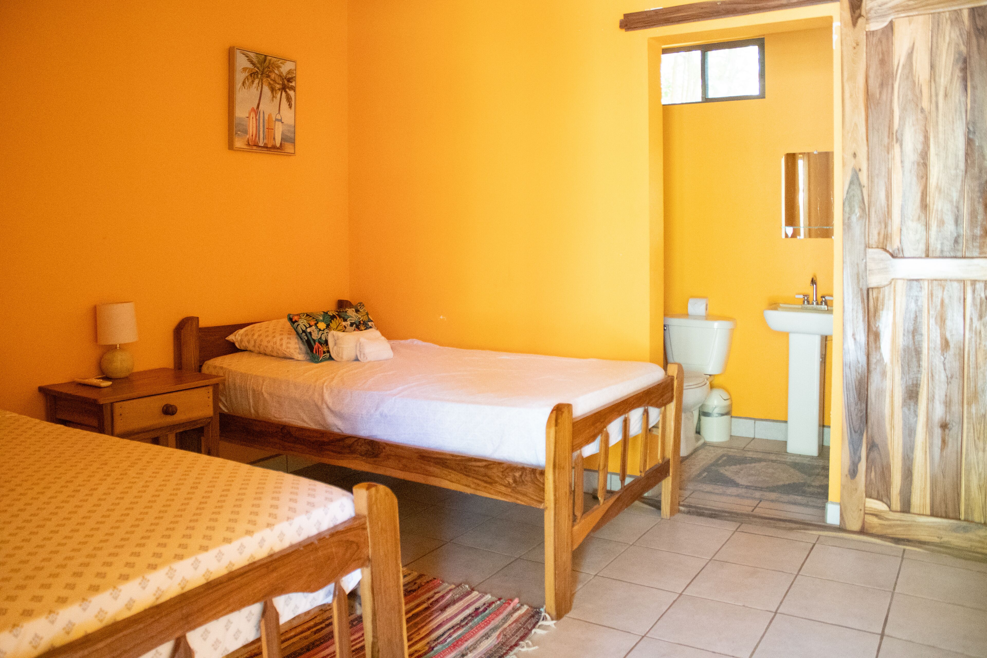 Una habitación con cama, mesita de noche, una pequeña mesa y baño con inodoro y lavamanos.